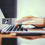 Hand typing on a laptop with a search bar overlay, representing changing a business domain name