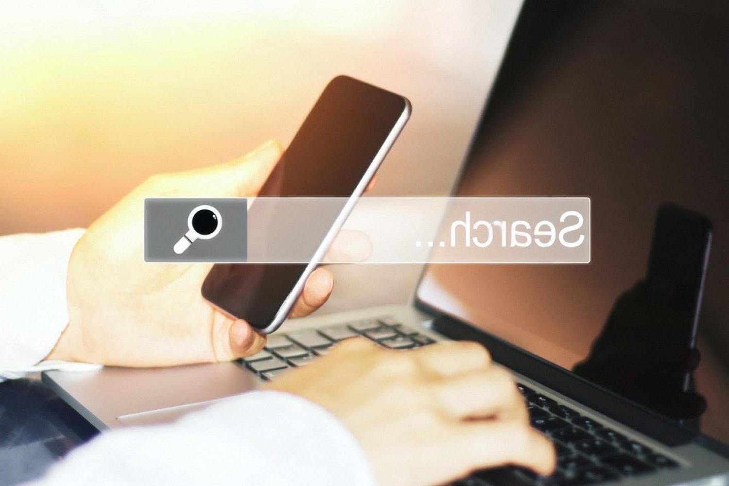 Person holding a smartphone next to a laptop with a search bar, researching a new domain name